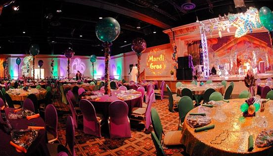 A room with tables and chairs, a stage and balloons.