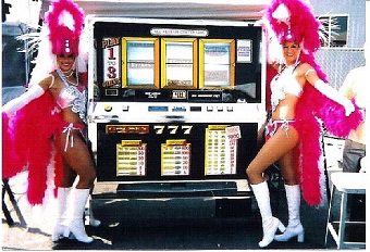 Two women in pink costumes standing next to a slot machine.